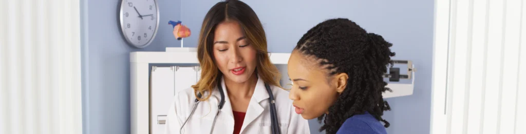A doctor in a white coat discusses anal cancer screening with a patient in an exam room, with a clock and anatomical model visible in the background, highlighting the importance of anoscopy for early detection in DC.