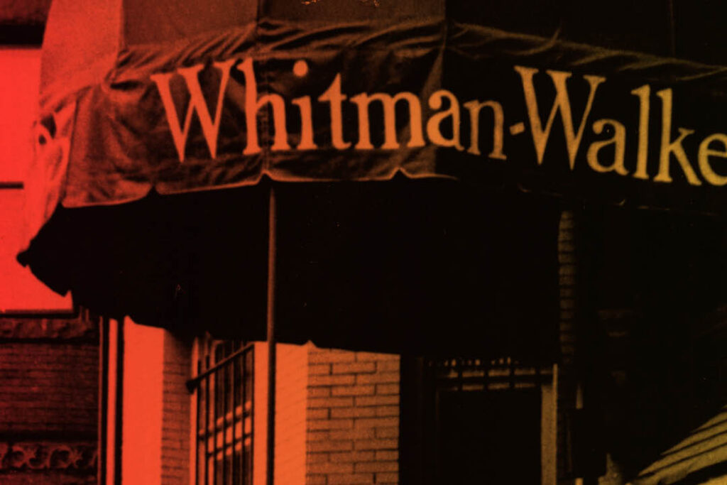 A red-tinted photo shows part of an awning with the text "Whitman-Walker" above a building with brick walls and a window.