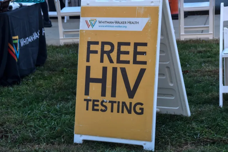 A yellow sign on grass reads "FREE HIV TESTING" with the Whitman-Walker Health logo and website at the top, promoting PrEP awareness as part of their healthcare leadership initiative.
