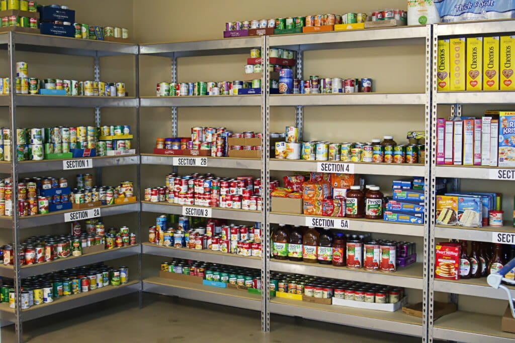 Metal shelving units in a D.C. food pantry, organized by numbered sections and stocked with canned goods, cereal, pasta, and jars of sauce to help residents keep benefits as food insecurity grows.