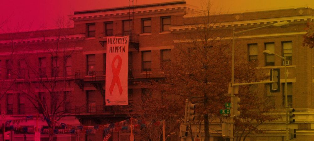 A large building displays a banner with a red ribbon and the words "MIRACLES HAPPEN"; autumn trees and street signs are visible in front.