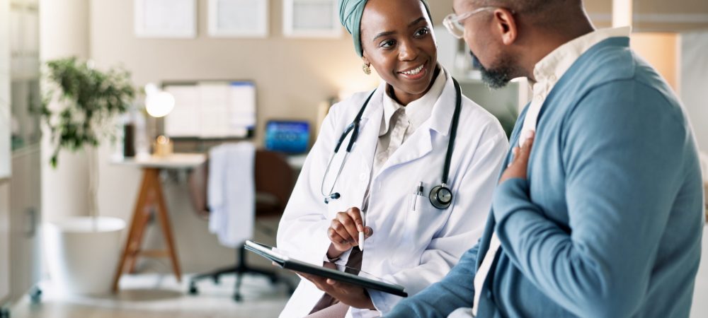 A doctor wearing a white coat and stethoscope consults with a patient in an office, both engaged in conversation as the doctor holds a clipboard to discuss HIV treatment updates 2025.