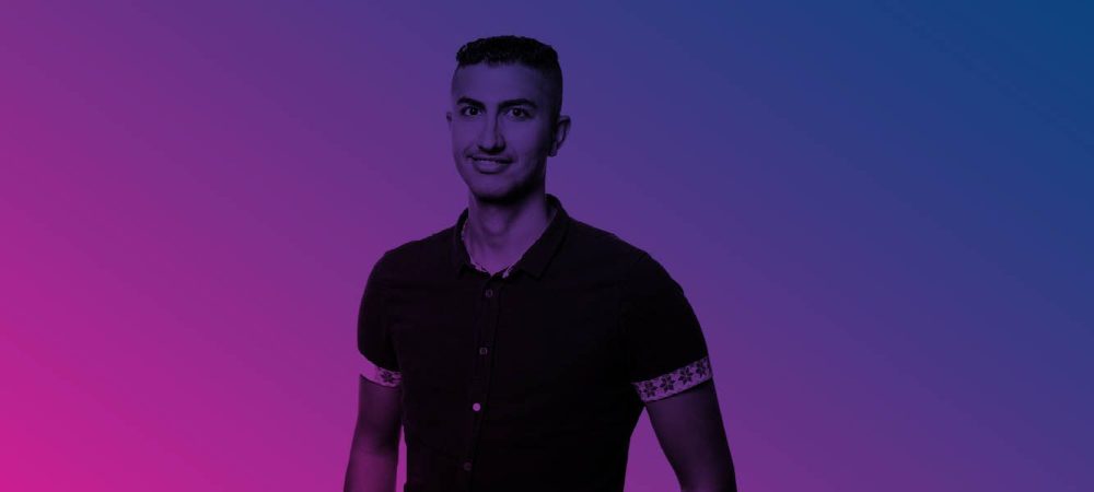 A person with short hair and a button-up shirt stands against a pink and blue gradient background.