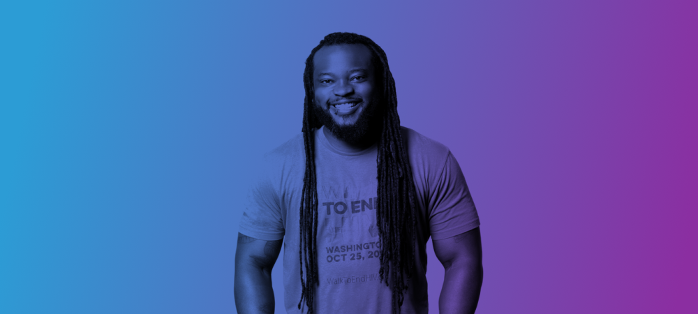 A person with long hair and a beard smiles while standing against a blue-to-purple gradient background.