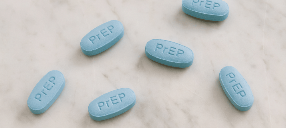 Six blue oval pills with “PrEP” imprinted on them are arranged on a white marble surface.