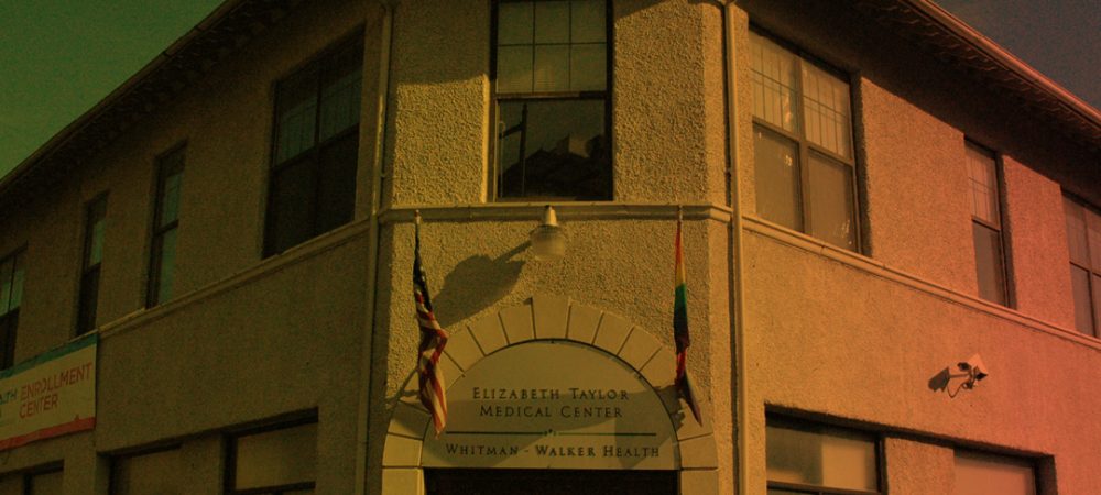 A two-story building with a sign reading "Elizabeth Taylor Medical Center, Whitman-Walker Health" above the entrance, with two flags displayed on either side of the door.