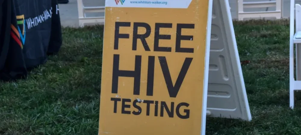 A yellow sign on grass reads "FREE HIV TESTING" with the Whitman-Walker Health logo and website at the top, promoting PrEP awareness as part of their healthcare leadership initiative.