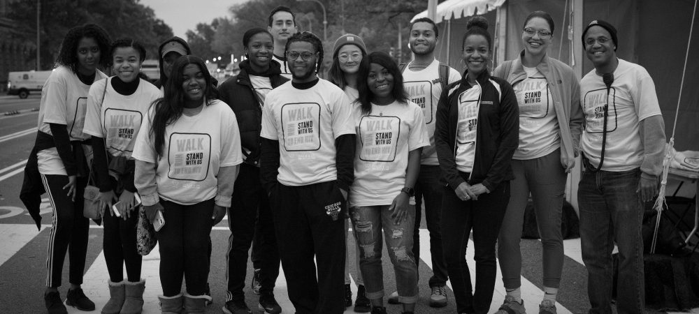 A group of people wearing matching "WALK to SHAW" shirts stand together and pose for a photo at an outdoor event near a tent.