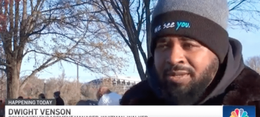 A man wearing a beanie and scarf speaks outdoors in a park during the Walk to End HIV; the caption identifies him as Dwight Venson, Community Engagement Manager at Whitman-Walker, featured in an NBC4 live shot.