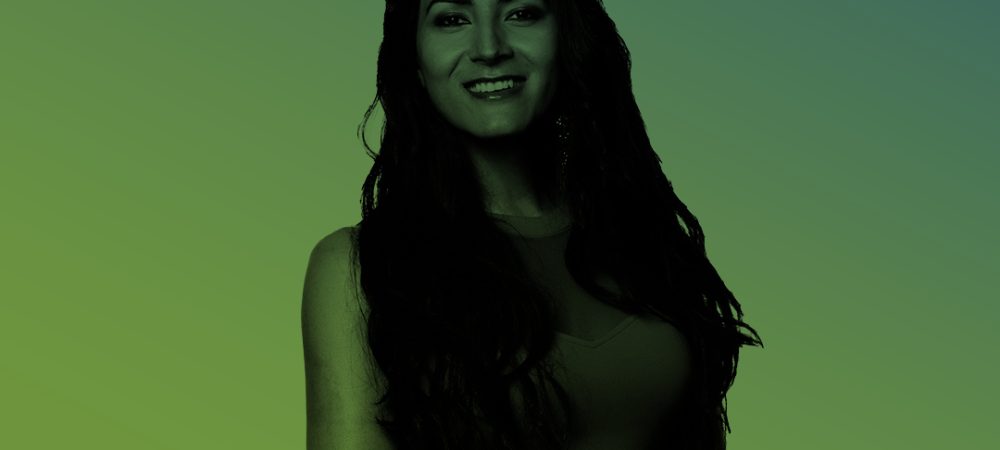 A woman with long dark hair stands smiling against a gradient green and blue background.