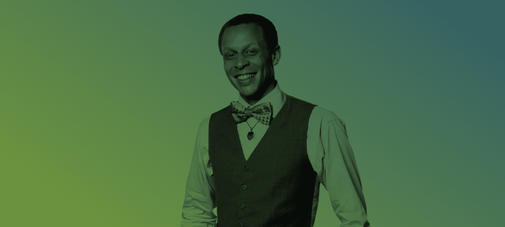 A man wearing a bow tie, vest, and collared shirt stands and smiles against a green gradient background.