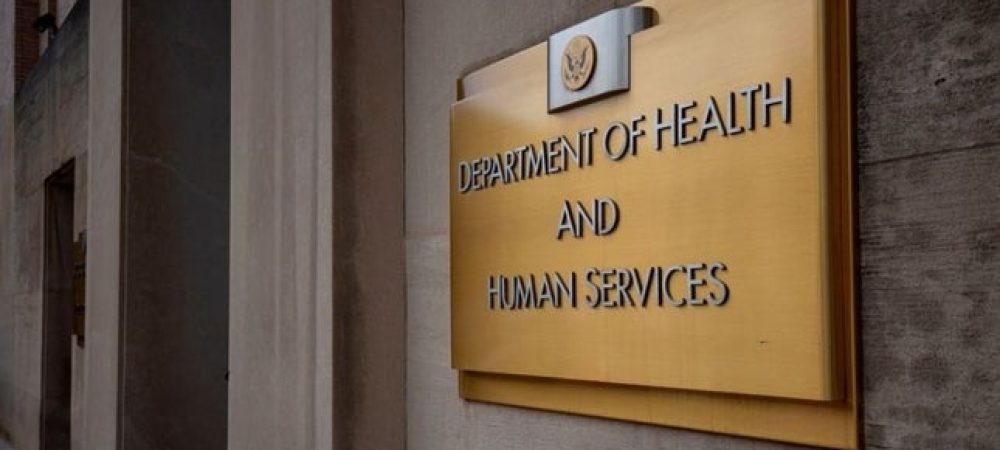 A gold sign on a stone building reads "Department of Health and Human Services" with the U.S. government seal above the text.